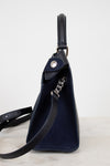 Navy blue leather bag with a chain detail strap on a light gray background