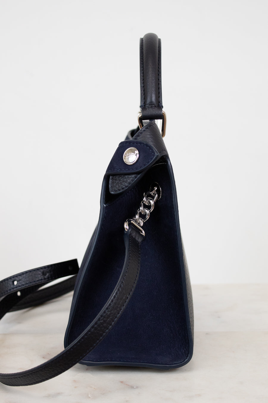 Navy blue leather bag with a chain detail strap on a light gray background