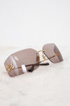 Miu Miu rimless sunglasses with gold metal frames and brown-tinted lenses, resting on a white marble surface.