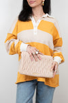 Woman holding a beige quilted clutch against a plain background