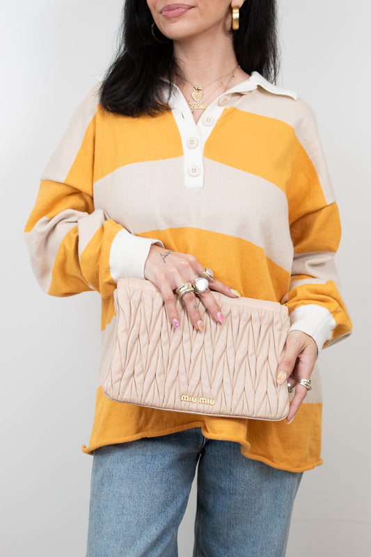 Woman holding a beige quilted clutch against a plain background