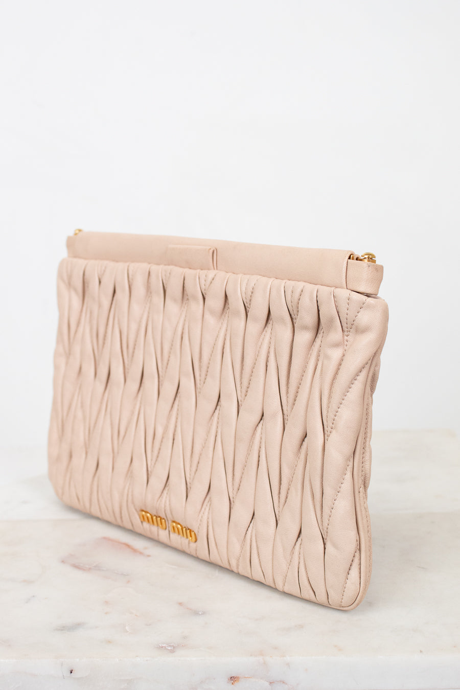 Beige clutch bag with textured pattern and 'miu miu' branding on a light background