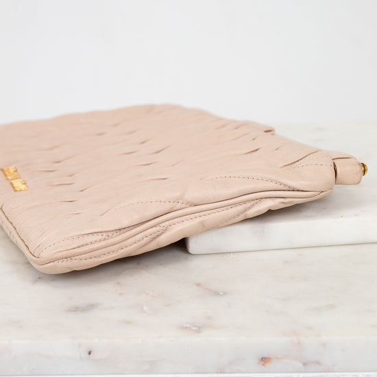 Beige quilted clutch bag on a marble surface with a white background