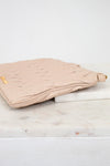 Beige quilted clutch bag on a marble surface with a white background