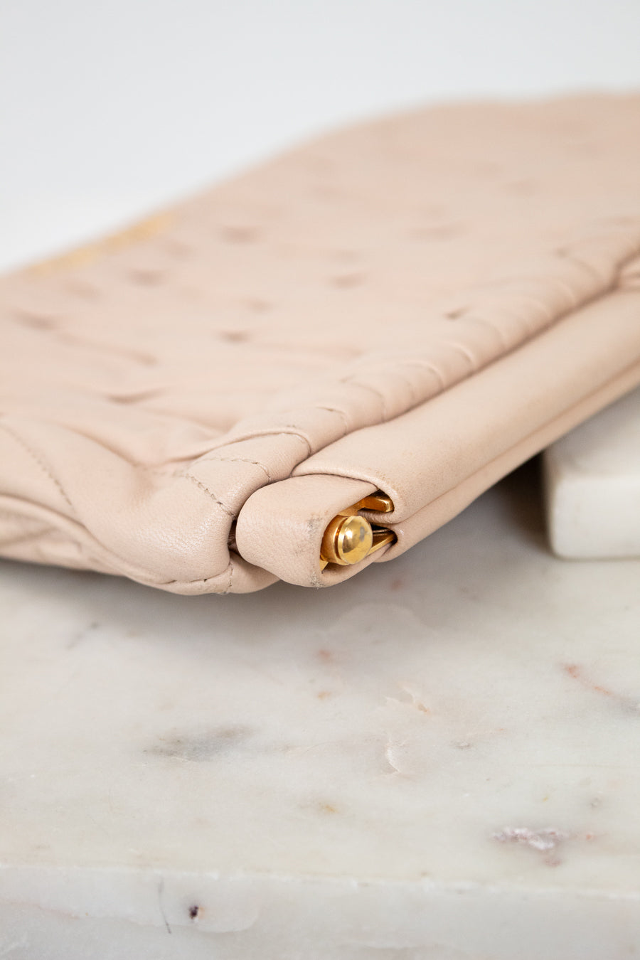 Beige quilted handbag with gold clasp on a marble surface