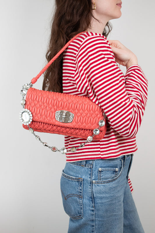 Person wearing a red and white striped shirt holding a coral handbag with decorative elements.