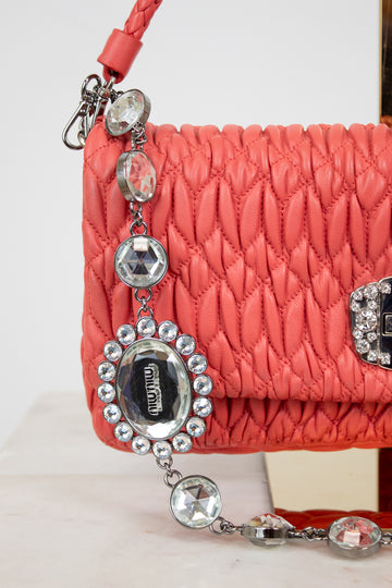 Coral quilted handbag with decorative chain and Miu Miu logo on a light background