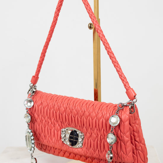 Coral handbag with decorative chain and clasp on a stand against a white background