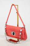 Coral handbag with decorative chain and clasp on a stand against a white background