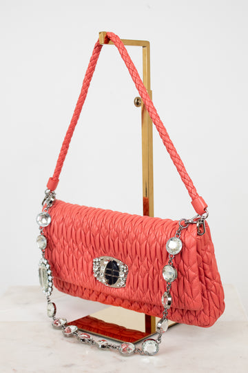 Coral handbag with decorative chain and clasp on a stand against a white background