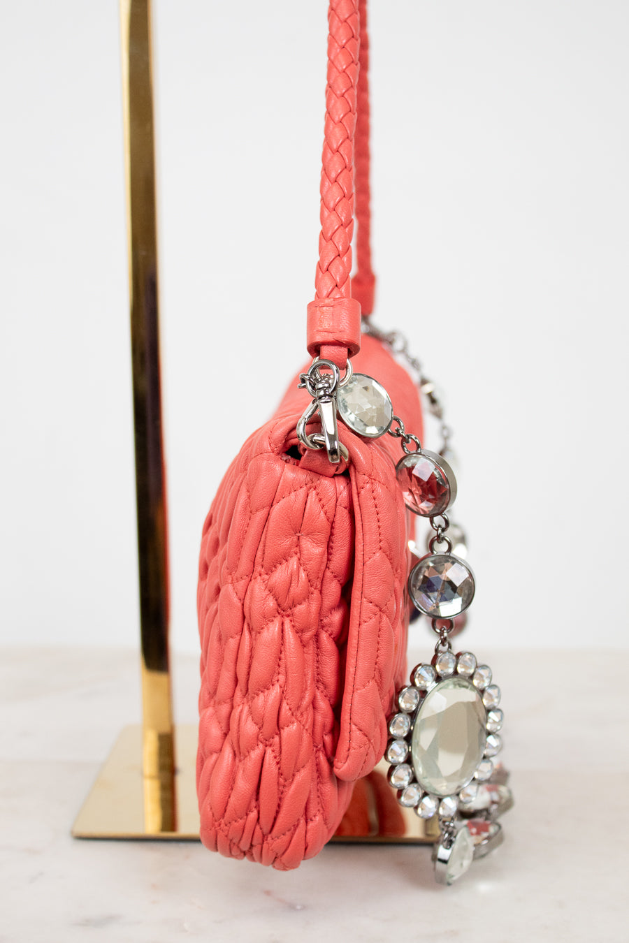 Coral shoulder bag with quilted design and decorative chain a white background