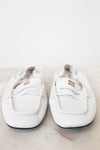 A pair of white leather Miu Miu loafers with gold branding, displayed on a light marble surface against a white background.