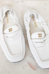 A pair of white Miu Miu leather penny loafers with gold branding, displayed on a light marble surface.