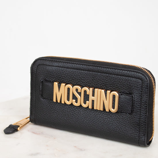 Black wallet with gold 'Moschino' logo on a white marble surface