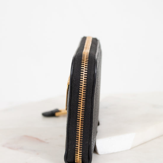 Black wallet with gold zipper on a white marble surface