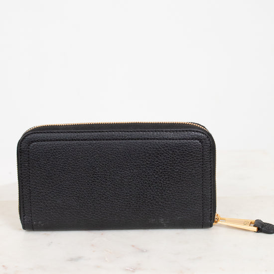 Black wallet with gold zipper on a white marble surface