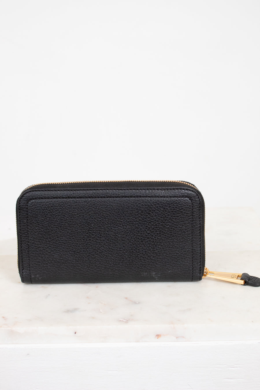 Black wallet with gold zipper on a white marble surface