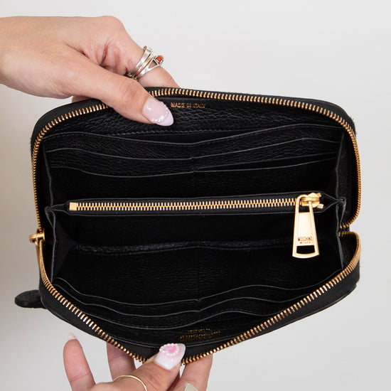 Hands holding open black wallet with gold zipper and card slots on white background 