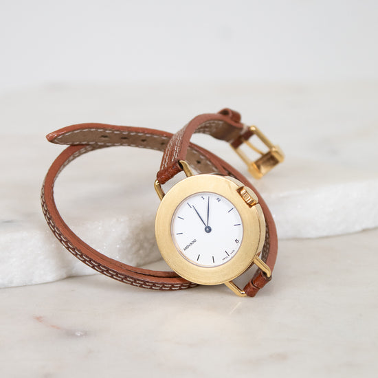 Gold watch with brown leather strap on a marble surface