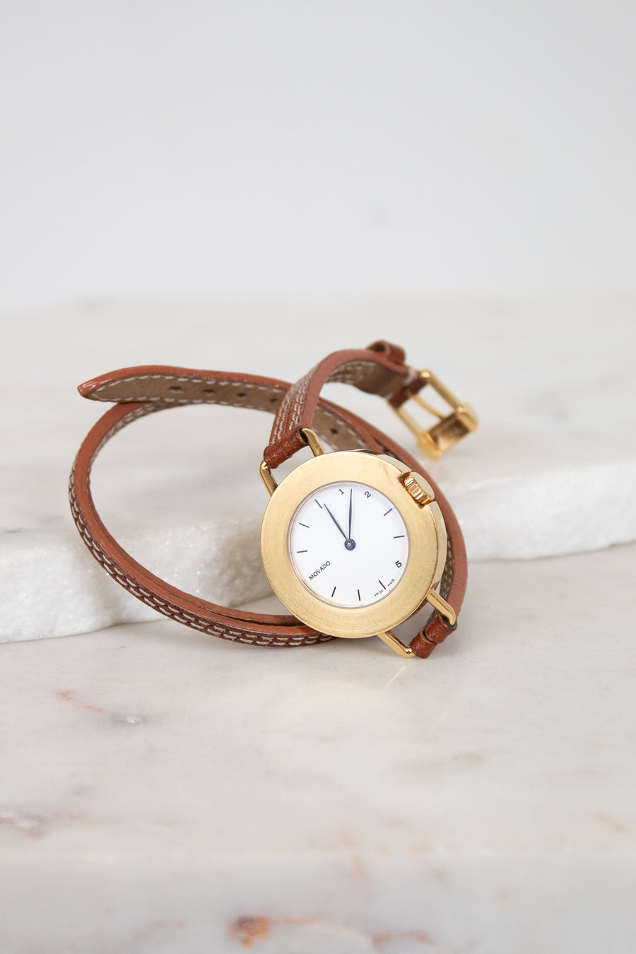 Gold watch with brown leather strap on a marble surface