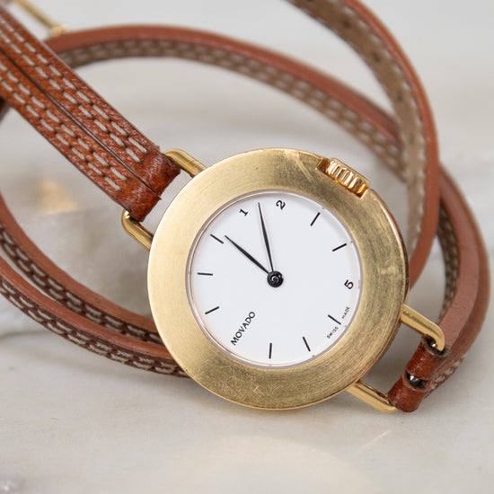 Gold watch with a brown leather strap on a light background