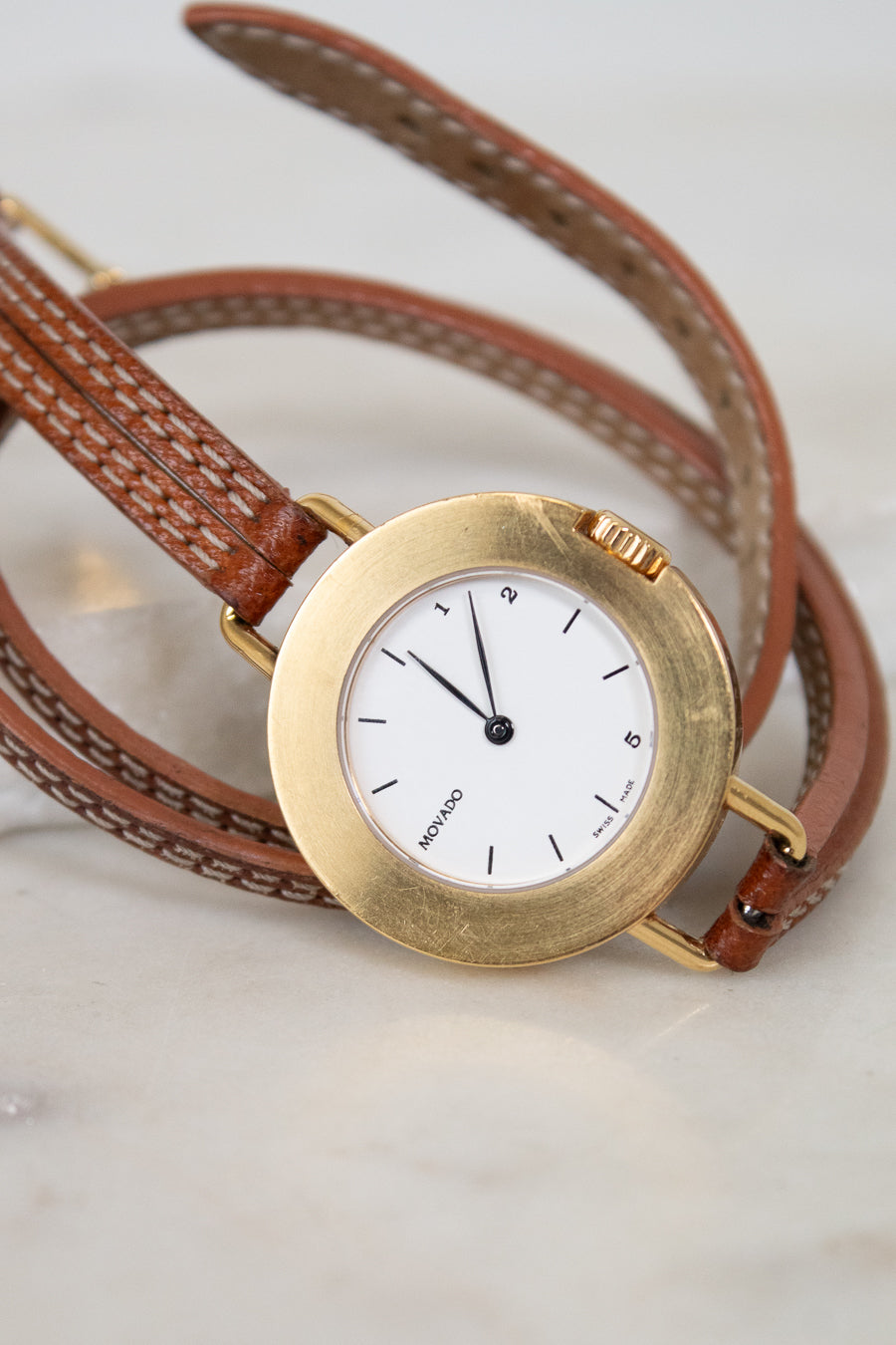 Gold watch with a brown leather strap on a light background