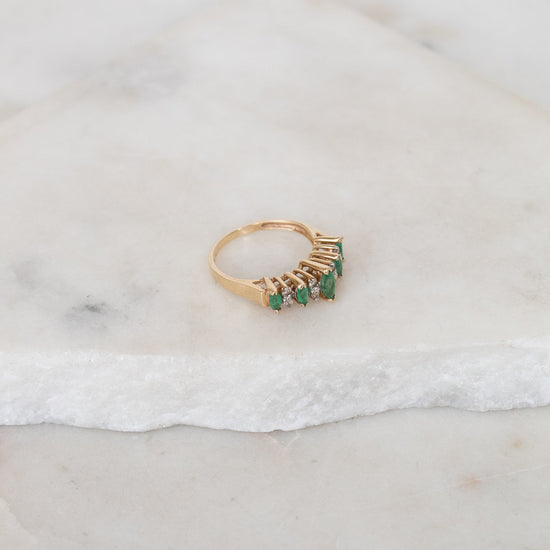 Gold ring with green gemstones on a marble surface