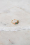 Gold ring with green gemstones on a marble surface