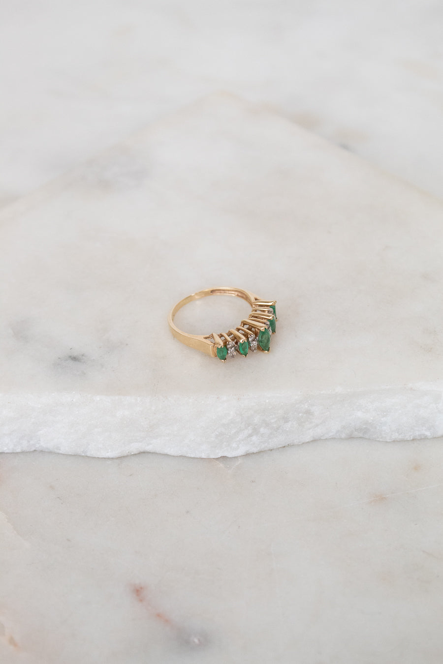 Gold ring with green gemstones on a marble surface
