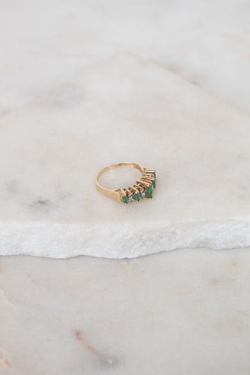 Gold ring with green gemstones on a marble surface