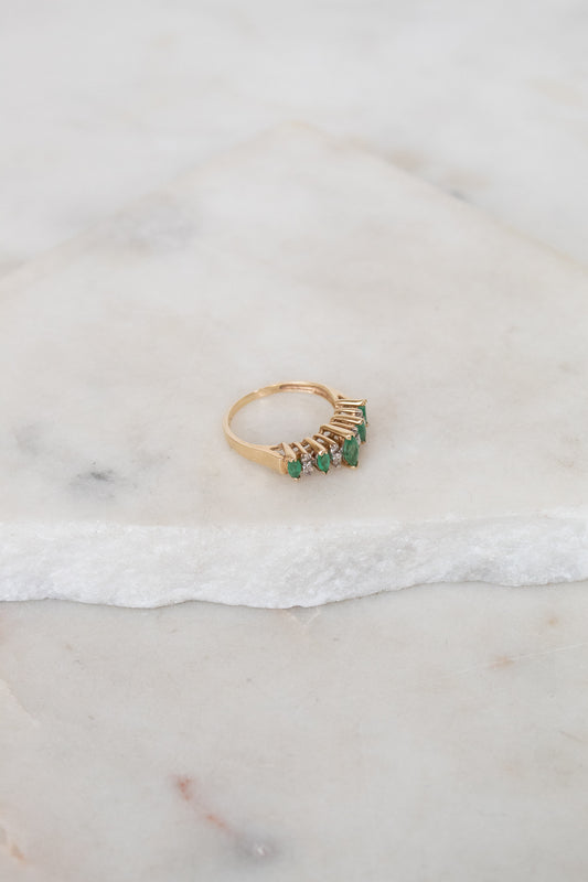 Gold ring with green gemstones on a marble surface