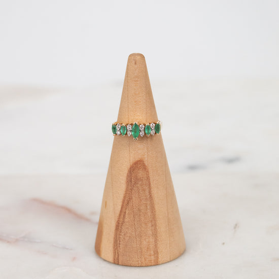 Ring with green gemstones on a wooden ring stand against a white background