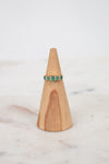 Ring with green gemstones on a wooden ring stand against a white background