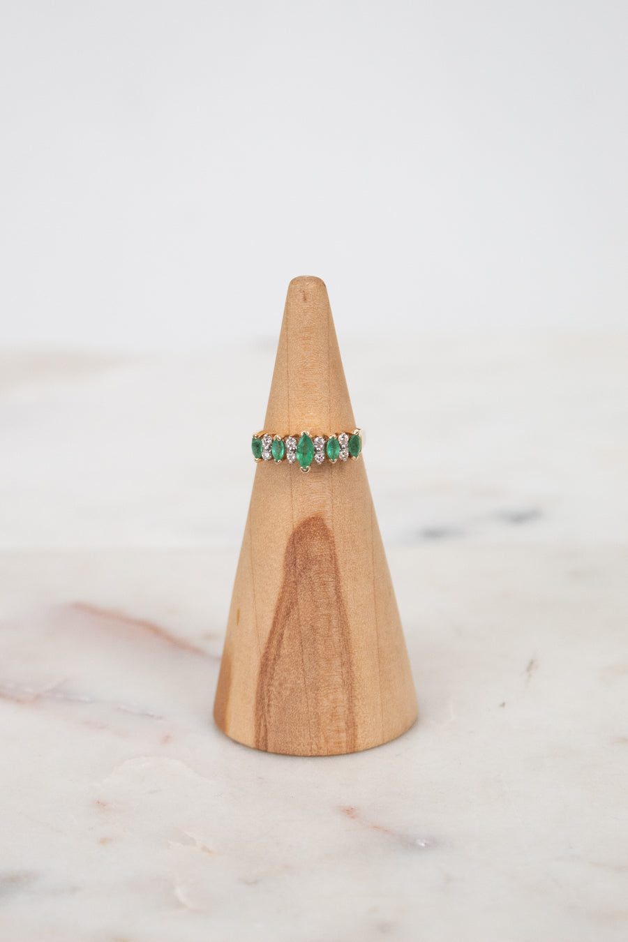 Ring with green gemstones on a wooden ring stand against a white background
