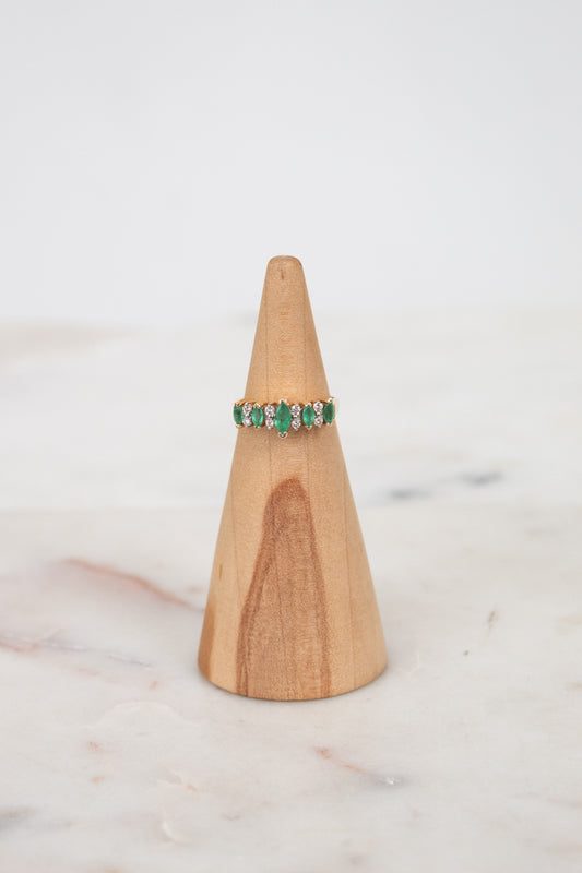 Ring with green gemstones on a wooden ring stand against a white background