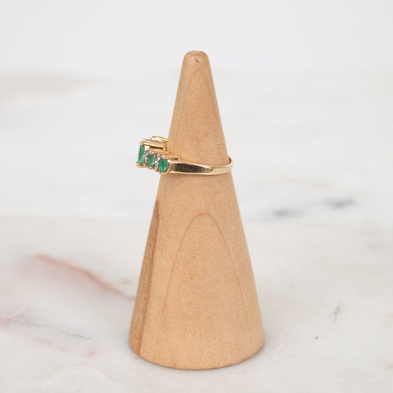 Gold ring with green gemstone on a wooden ring stand against a marble background