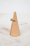 Gold ring with green gemstone on a wooden ring stand against a marble background