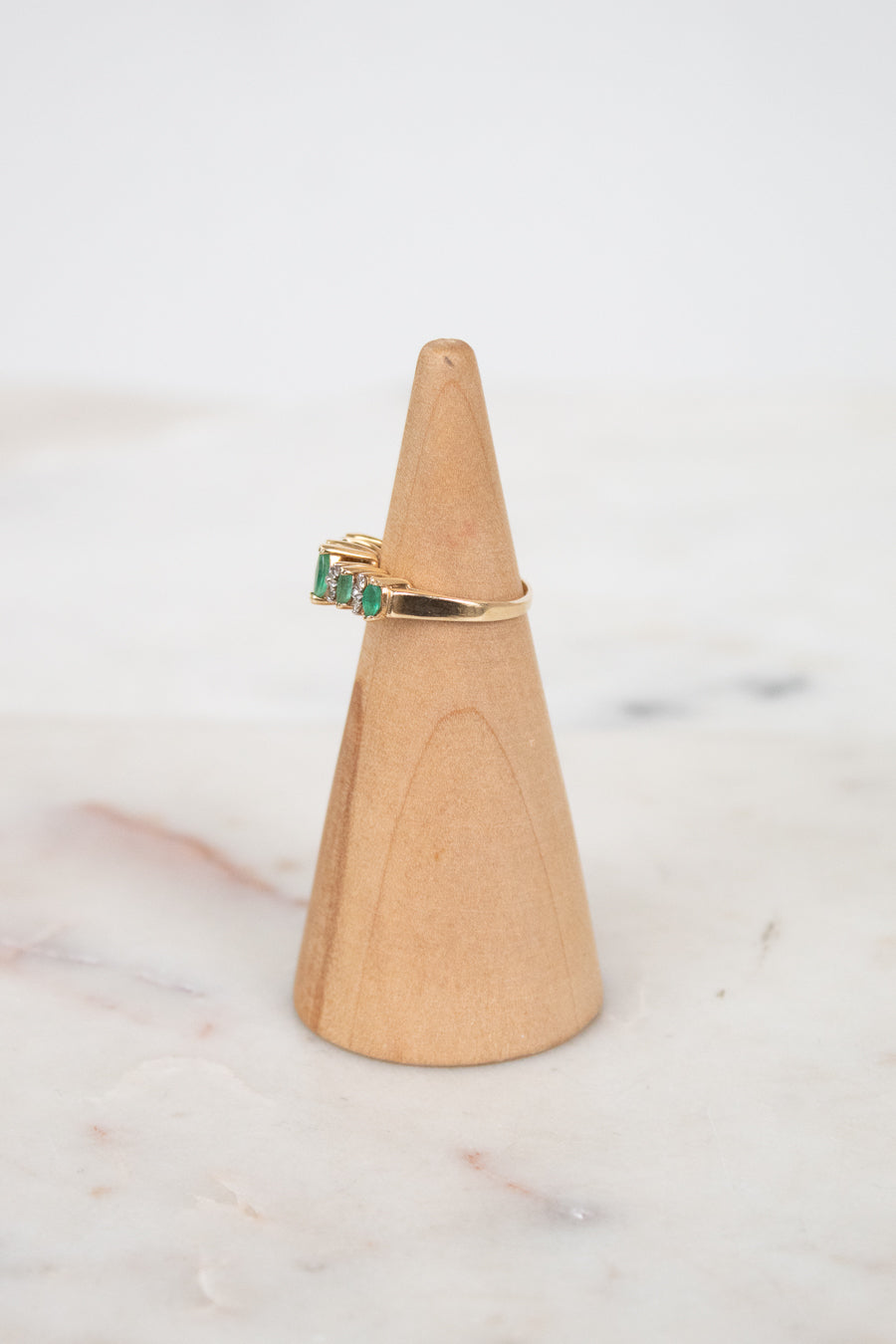 Gold ring with green gemstone on a wooden ring stand against a marble background