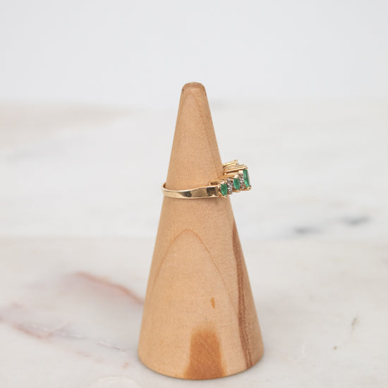 Gold ring with green gemstone on a wooden ring stand against a marble background