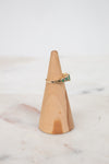 Gold ring with green gemstone on a wooden ring stand against a marble background