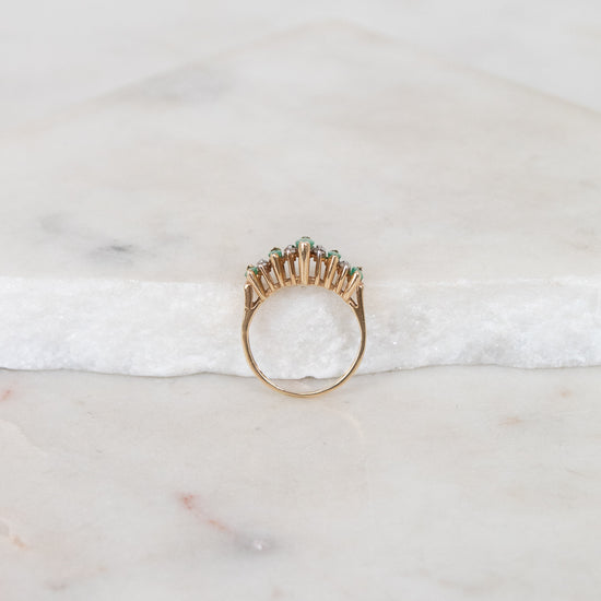 Gold ring with green stones on a marble surface