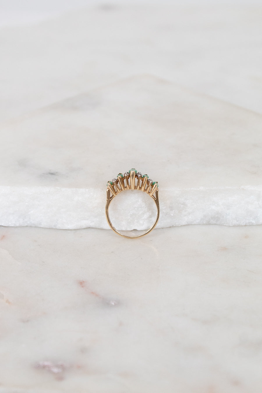 Gold ring with green stones on a marble surface