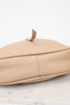 Beige leather handbag on a marble surface with a white background