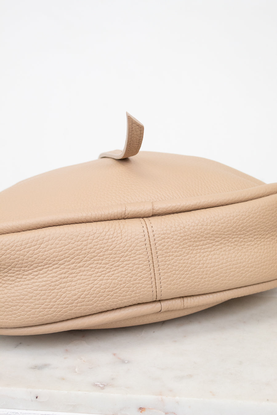 Beige leather handbag on a marble surface with a white background