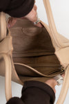 Close-up of a person opening a beige handbag with a brown interior.