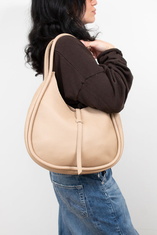 Person wearing a beige shoulder bag against a white background