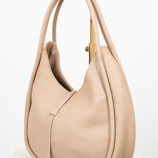 Beige handbag sitting on a gold purse stand on a white background
