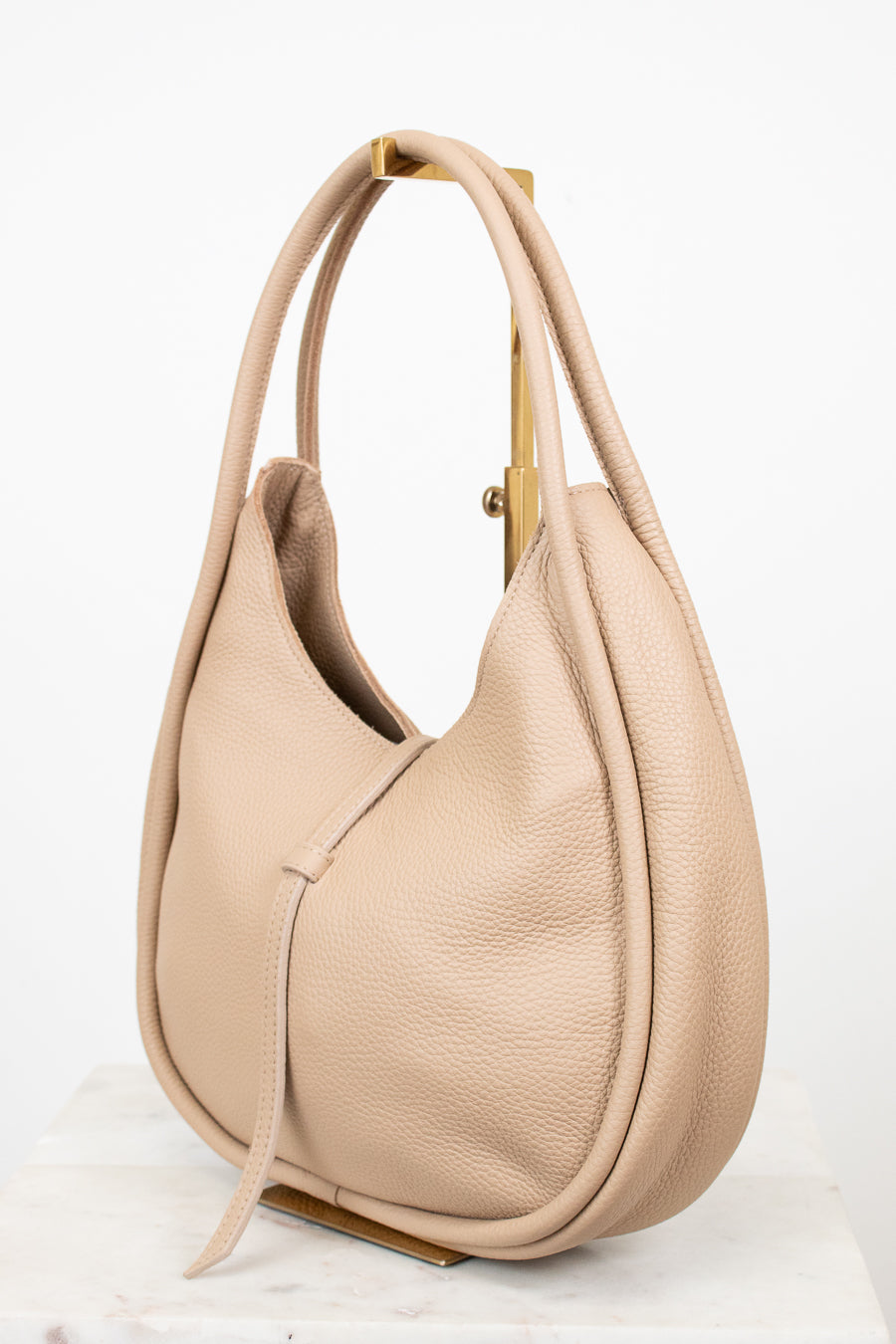 Beige handbag sitting on a gold purse stand on a white background