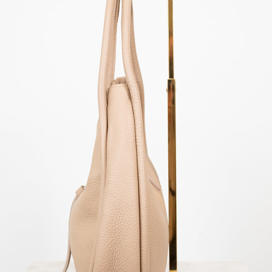 Beige handbag hanging on a gold stand against a white background