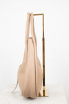 Beige handbag hanging on a gold stand against a white background